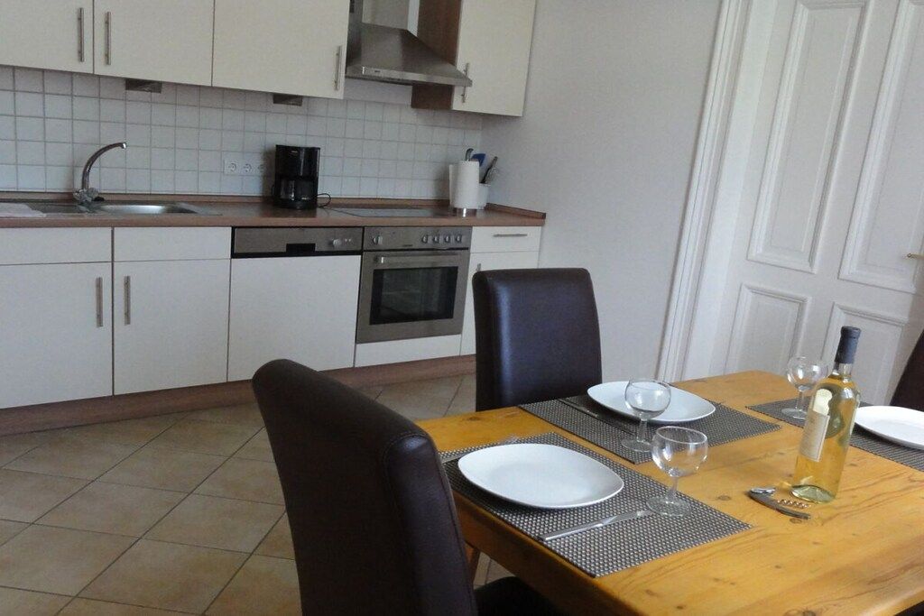 Ein Essbereich mit einem Holztisch, gedeckt für zwei Personen, einer Weinflasche und einer Kaffeemaschine auf der Arbeitsplatte.