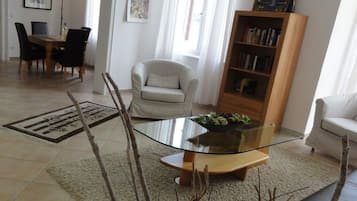 Un soggiorno con un tavolino in vetro, una poltrona bianca, una libreria e un'area pranzo con sedie e tavolo.