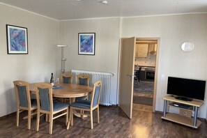 Ein Essbereich mit einem runden Tisch, Stühlen, einem Heizkörper, einer Uhr und einem Fernseher auf einem Schrank.