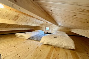 A wooden attic bedroom with two beds, a window, and a wooden ceiling.