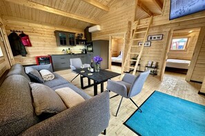 Interior acogedor de una cabaña con sofá, sillas, una mesa de comedor y una zona de cocina.