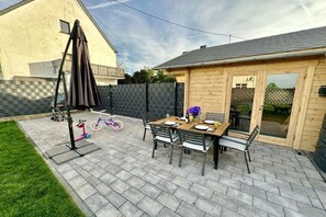 A patio with a table set for two, surrounded by chairs, a folding table, and a bicycle.