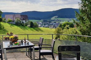 A terrace with a table and chairs overlooking a valley with houses and greenery. - Panoramic view of Baiersbronn (Baiersbronn)