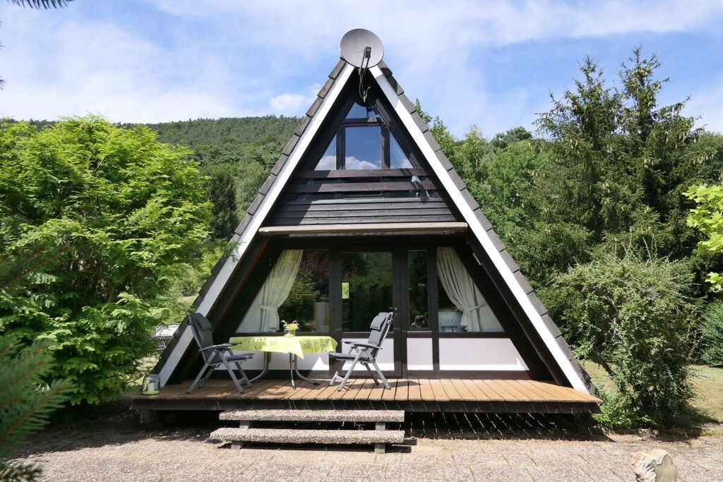 Une structure triangulaire en bois dotée d’un balcon, d’une table et de deux chaises.
