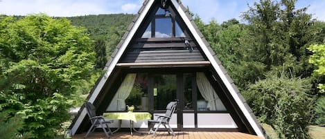 A triangular wooden structure with a balcony, a table, and two chairs.