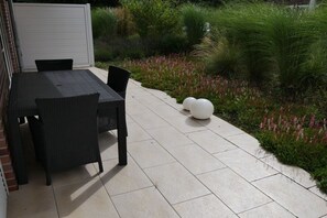 Eine Außenpatio mit Tisch und Stühlen, umgeben von einem Garten mit verschiedenen Pflanzen und Blumen.