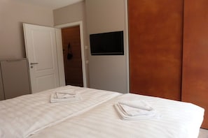 Ein Hotelzimmer mit einem Bett, einem an der Wand befestigten Fernseher und einer Tür zu einem weiteren Raum.