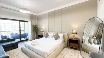A modern hotel room with a large bed, a sitting area with a bench, a large mirror, and a view of the city through the window.