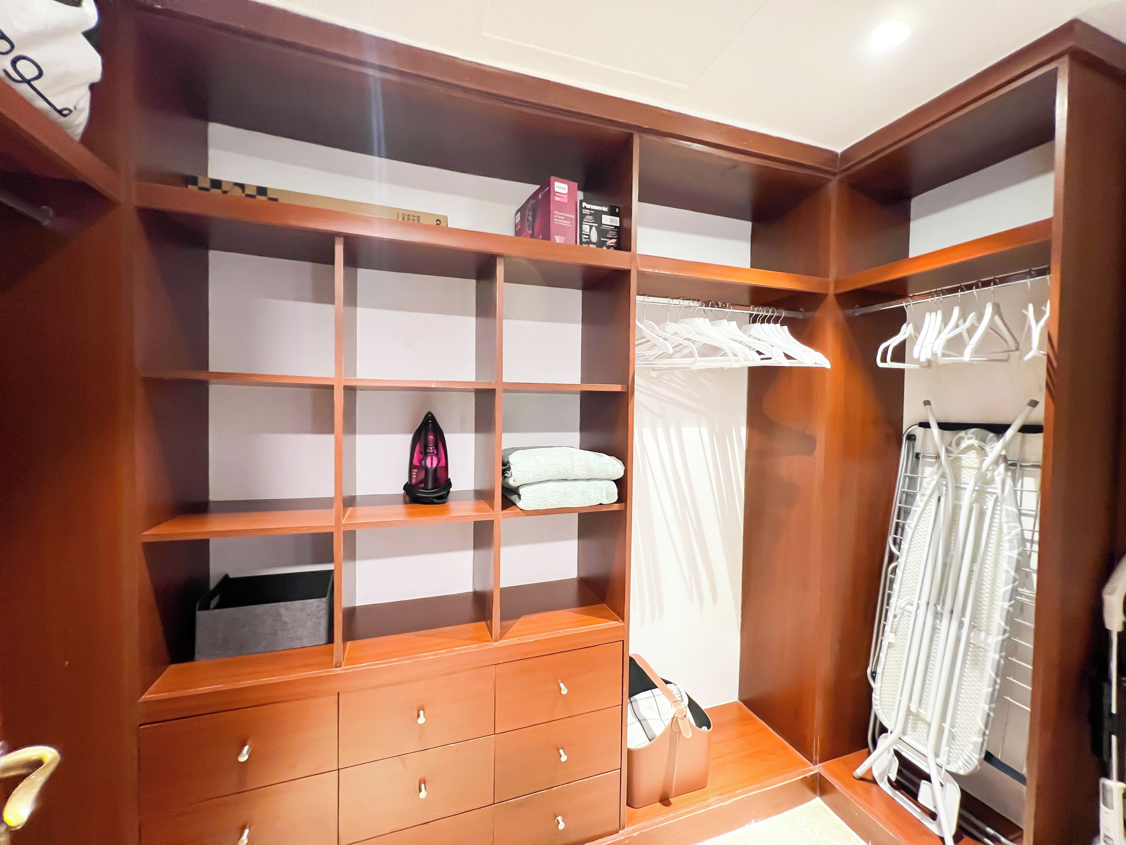 A walk-in closet with wooden shelving, a built-in iron, and a hanging rack.