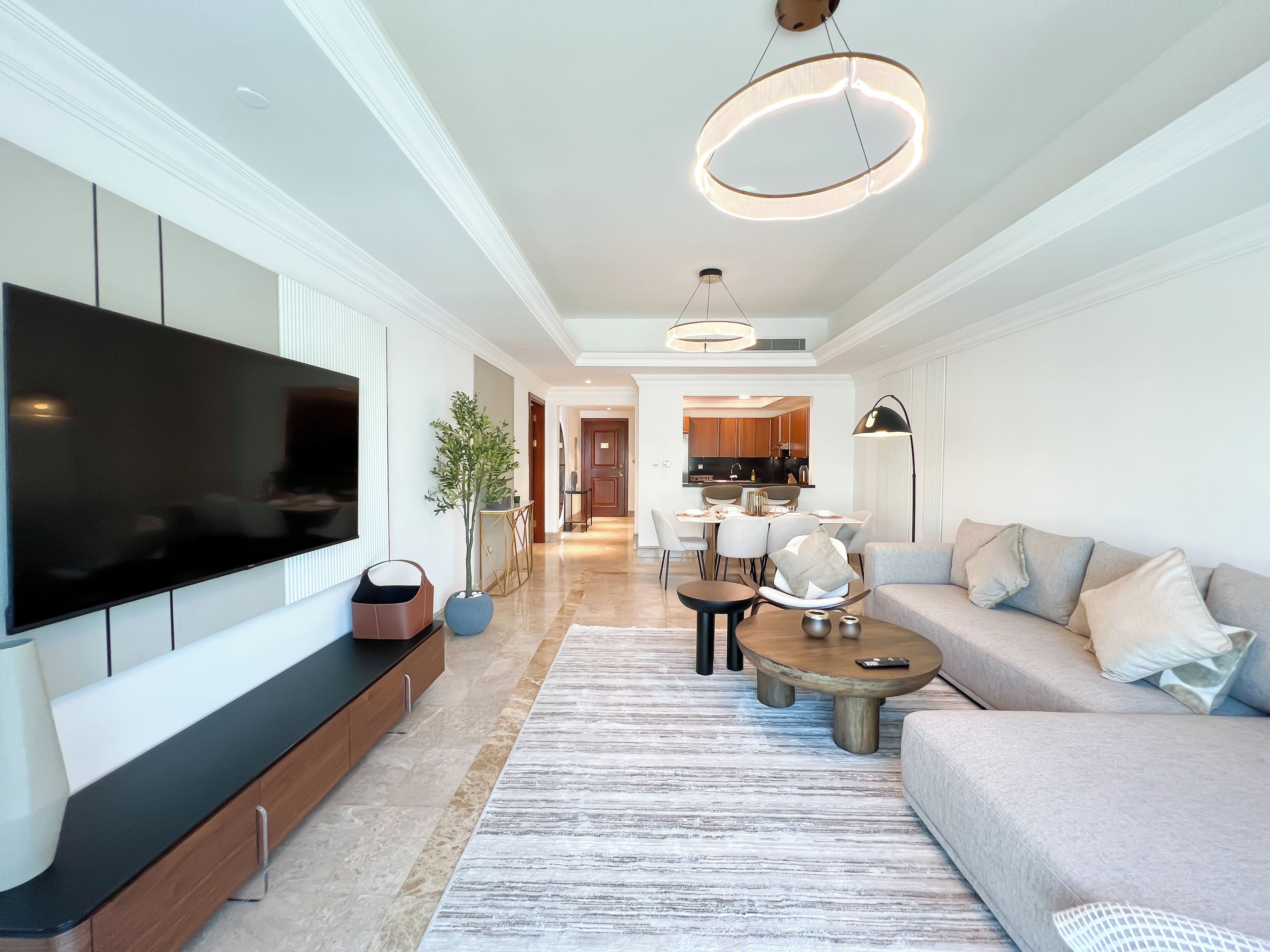 A modern living room with a flat-screen TV, a sofa, a coffee table, and a dining area with chairs and a table.