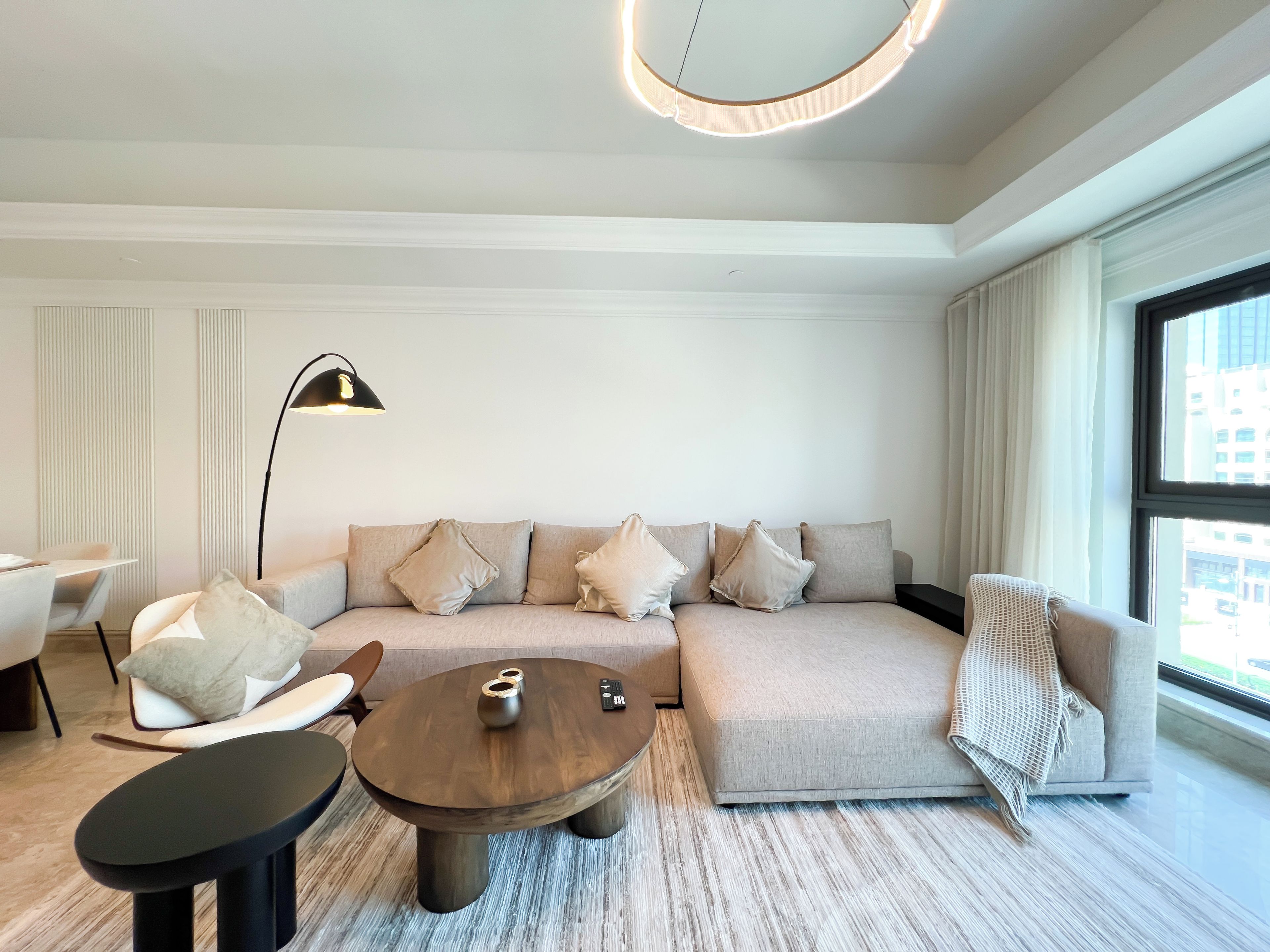 Un salon moderne avec un canapé d’angle, une table basse ronde et un lampadaire.