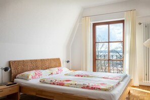 A bedroom with a wooden bed, a nightstand, a window with curtains, and a radiator. - La Perla - Longing for the Sea (Überlingen)