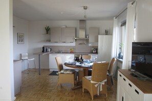A modern kitchen with a dining area, featuring a central island, white cabinetry, and a large window. - Holiday home with 3 bedrooms (Brohl-Lützing)