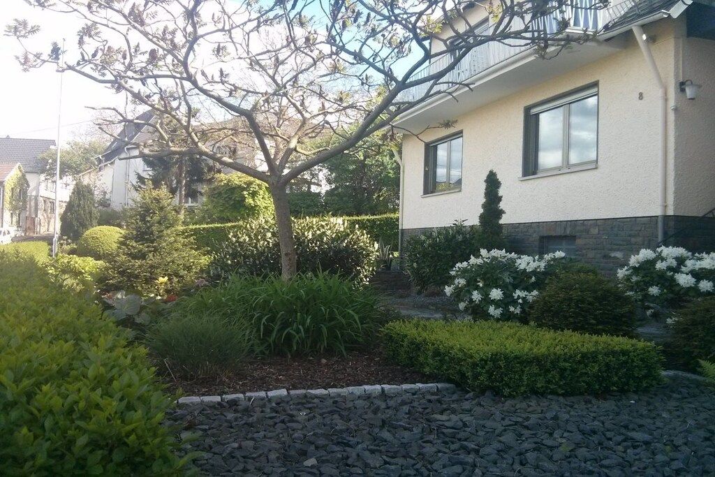Une maison d’habitation avec un jardin, un arbre et un chemin pavé de pierres.