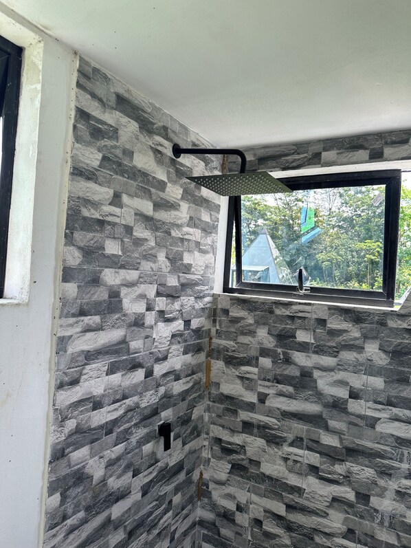 A bathroom with a stone wall, a window, and a showerhead.