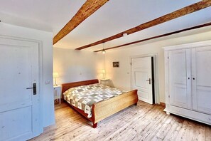 Ein Schlafzimmer mit Holzbalkendecke, einem Bett mit gemustertem Überwurf, einem Kleiderschrank und einem Nachttisch mit Lampe.