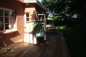 Un patio in legno con una sedia a righe verdi, un tavolo e una scopa appoggiata a un muro in mattoni.