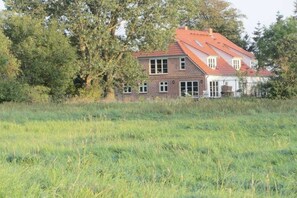 Ein zweistöckiges Haus mit rotem Dach, umgeben von einer grünen Wiese und Bäumen.
