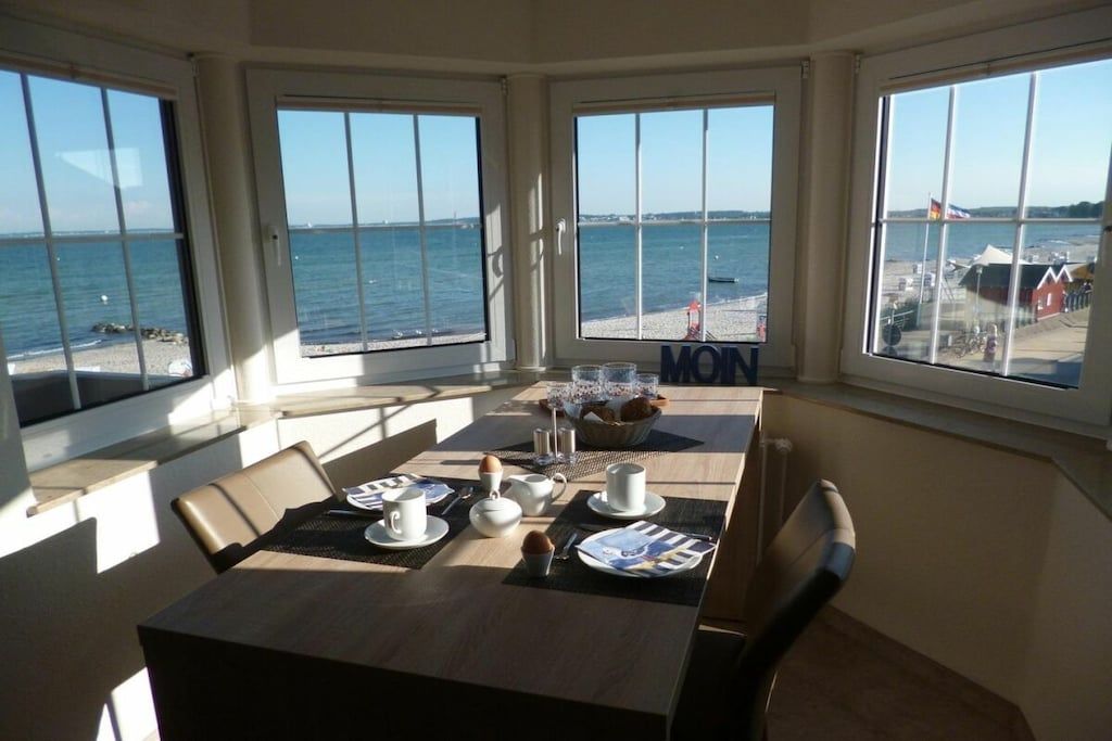 A dining area with a table set for breakfast, overlooking a beach.