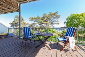 A wooden deck with two striped chairs and a table, overlooking a clear sky and trees. - Holiday apartment in Binz with swimming pool (Binz)
