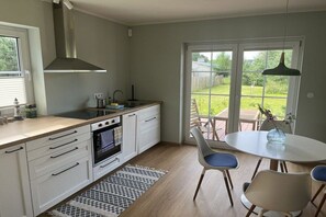 A modern kitchen with white cabinetry, a built-in oven, and a large window overlooking a garden. - Holiday apartment with 1 bedroom (Pruchten)