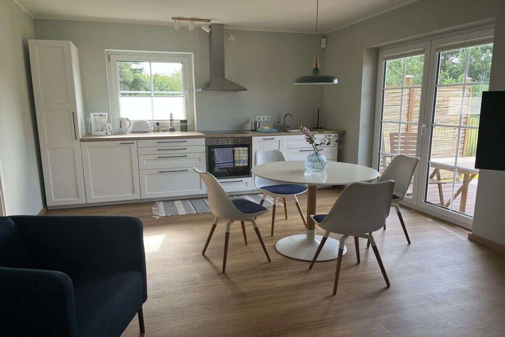 Una cocina moderna con armarios blancos, una mesa de comedor con sillas y un ventanal que proporciona luz natural.