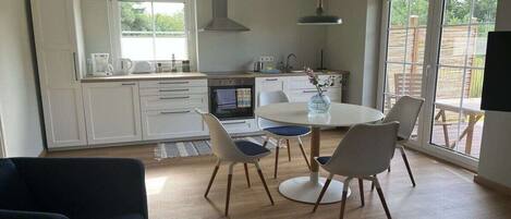 Una cocina moderna con armarios blancos, una mesa de comedor con sillas y un ventanal que proporciona luz natural.