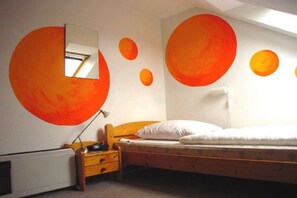 A bedroom with a bed, a nightstand, a lamp, and a wall with circular orange decorations. - Spacious holiday apartment in Petersdorf (Petersdorf\/Fehmarn)