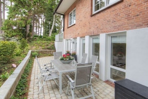 Eine Terrasse mit Tisch und Stühlen, umgeben von einer Ziegelmauer und Grünpflanzen.