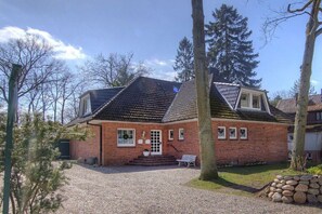 Ein Backsteinhaus mit geneigtem Dach, einer Veranda mit Stufen und einer Bank.