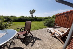 Ein Sitzbereich im Freien mit Tisch und Stühlen, einem Kiesgrund und einem Holzzaun im Hintergrund.
