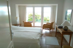 Ein Hotelzimmer mit einem Bett, einem Schreibtisch, einem Sessel und Blick durch eine Glasdoor.