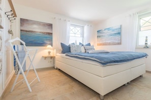 A bedroom with a bed, a nightstand, a lamp, and artwork on the walls. - Holiday apartment in Zingst with Wi-Fi (Zingst)
