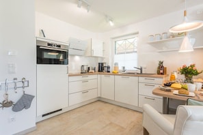 A modern kitchen with white cabinetry, a built-in oven, and a dining area with a table and chairs. - Holiday apartment in Zingst with Wi-Fi (Zingst)