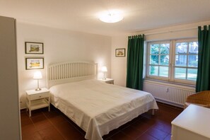 Una camera da letto con un letto, due comodini con lampade, una finestra con tende e un termosifone.
