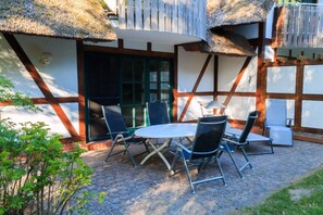 Un patio con tavolo e sedie, un tetto di paglia e un edificio in legno con una finestra.