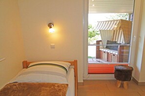 Een kamer met een bed, een wandlamp, een klein krukje en uitzicht op een zitgedeelte buiten via een glazen deur.