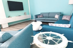 A living room with a teal sofa set, a white coffee table with a ship wheel, and a flat-screen TV mounted on the wall. - Holiday apartment with 2 bedrooms (Sassnitz)