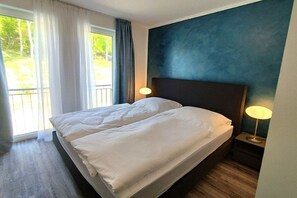 Ein Hotelzimmer mit einem Bett, zwei Nachttischlampen, Blick auf Grünfläche und einer blauen Akzentwand.