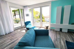 A modern living room with a blue sofa, large windows, and a view of the outdoors. - Holiday apartment with 2 bedrooms (Sassnitz)