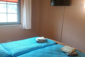 Een kamer met twee bedden, een raam met gordijn en een aan de muur bevestigde televisie.
