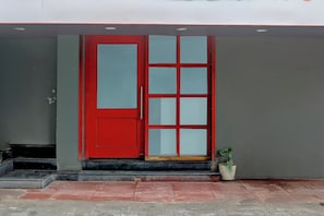 A red door with a glass panel, a small potted plant, and a concrete staircase leading to the entrance.