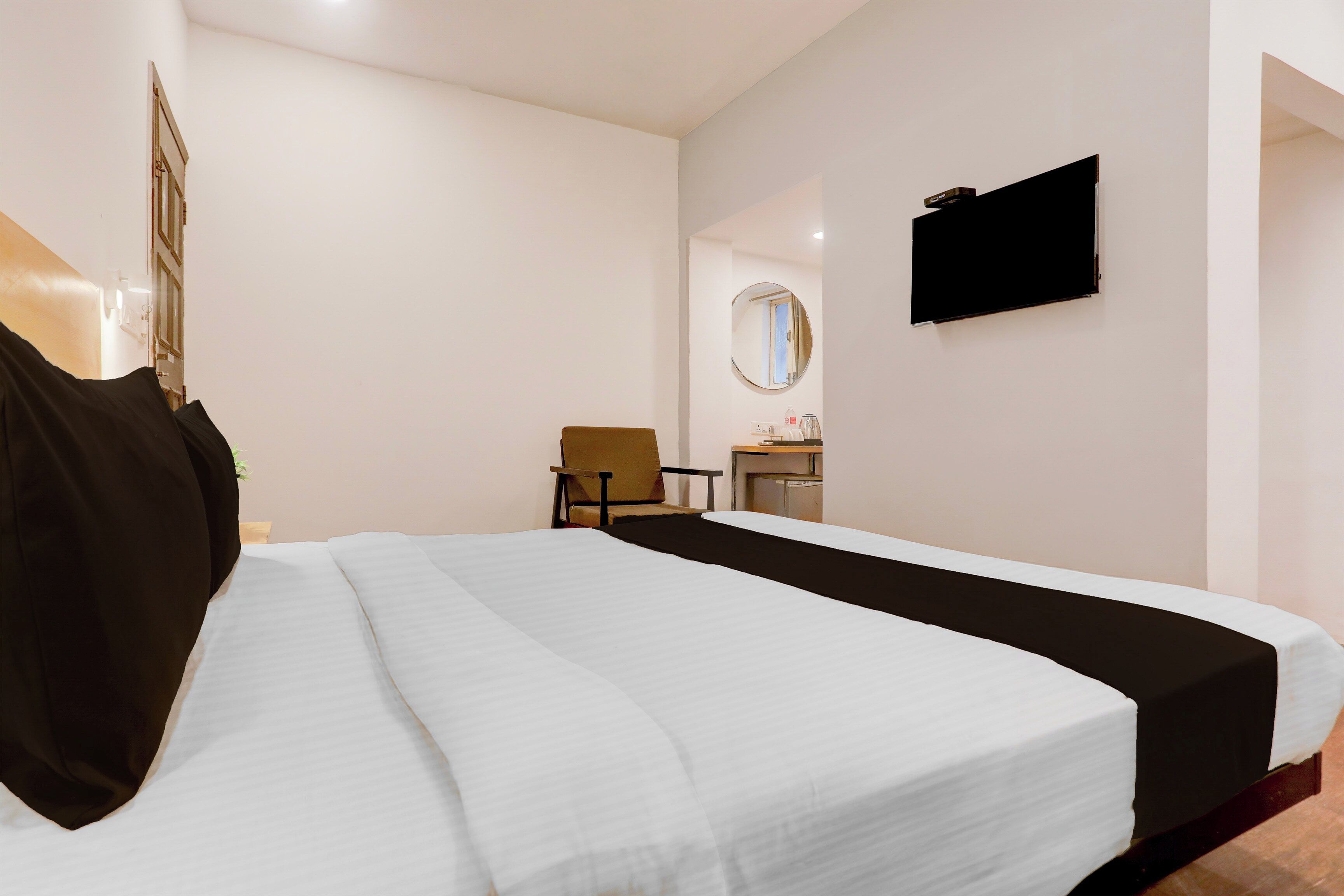 Habitación de hotel con cama, una silla, un escritorio con espejo y televisión en la pared.