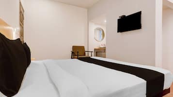 Ein Hotelzimmer mit Bett, Sessel, Schreibtisch mit Spiegel und Fernseher an der Wand.