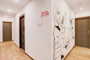 A hotel corridor with wooden flooring, doors numbered 205 and 208, and a wall mural.