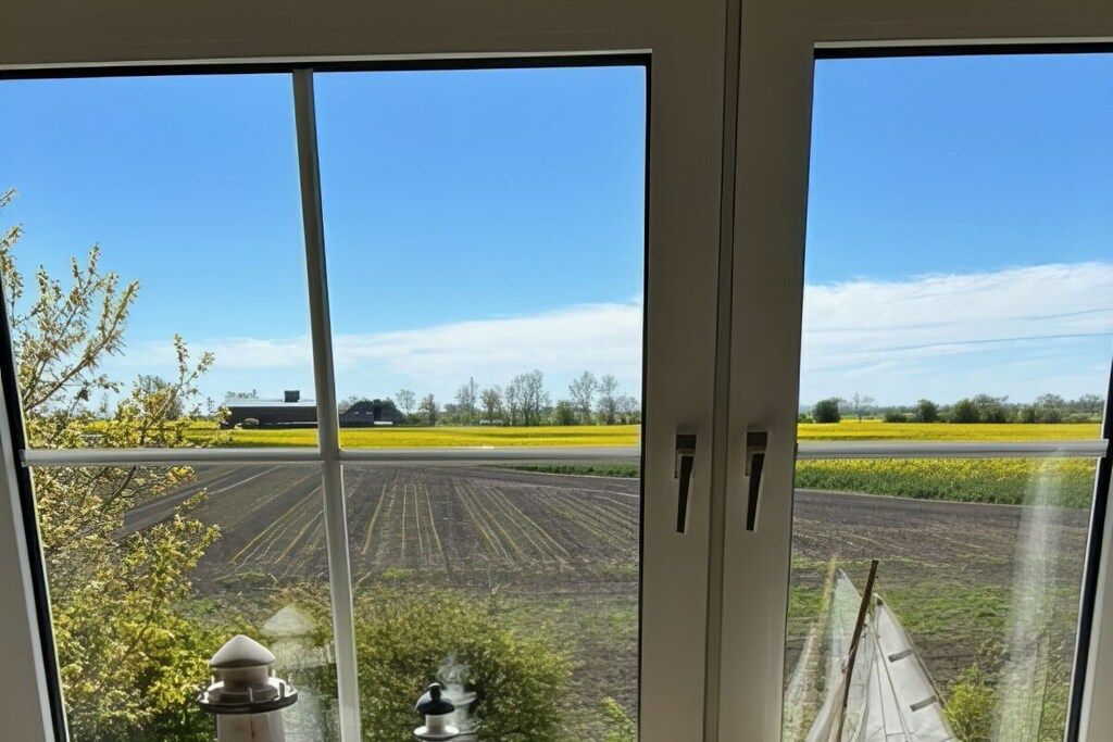 A view through a window with a rural landscape, including fields and a distant building.