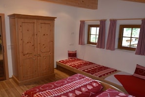 Une chambre avec deux lits simples, une armoire en bois et une fenêtre avec des rideaux.