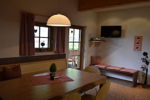 Et spiseområde med et træbord, stole, en bænk og et tv ophængt på væggen.