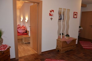 A room with a wooden door, a bed with red bedding, a small wooden chest, and a wall with decorative items. - Holiday apartment with 1 bedroom (Hippach)