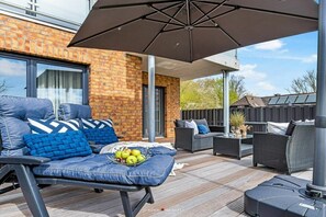 An outdoor patio with a sofa set, a table with fruit, and a large umbrella. - Holiday apartment at the marina (Damp)